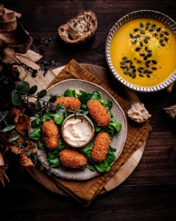A cozy dining setup featuring crispy croquetas served alongside a smooth pumpkin cream soup
