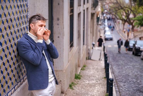 Man musician in a blue blazer and white sweater playing blues on a harmonica with eyes closed,