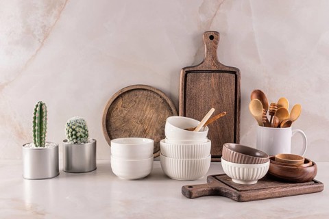 A well-arranged kitchen countertop featuring rustic wooden boards, ceramic bowls, wooden utensils,