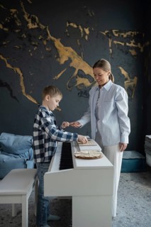 A young boy receives piano lessons from a smiling instructor in a modern, cozy room. The music