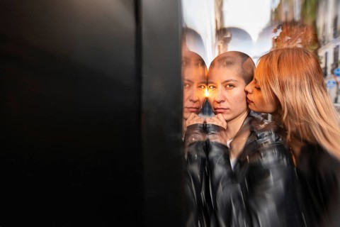 An intimate portrait of a lesbian couple sharing a tender moment, reflecting in glass. The artistic