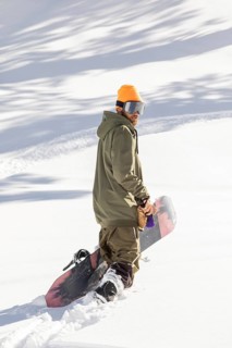 A snowboarder in an orange helmet and green jacket navigates through pristine powder in a remote