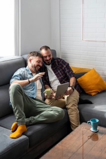 A smiling couple relaxes on a sofa, sharing a tablet. They enjoy each other's company in a cozy