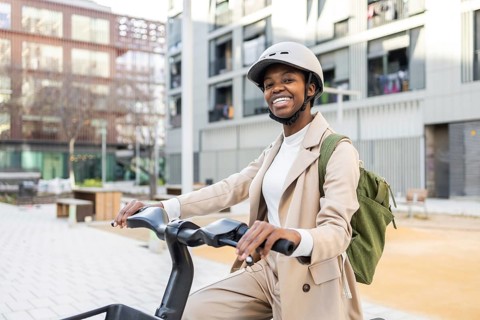 Black woman smiling while riding a bike in an urban city environment, wearing a helmet and