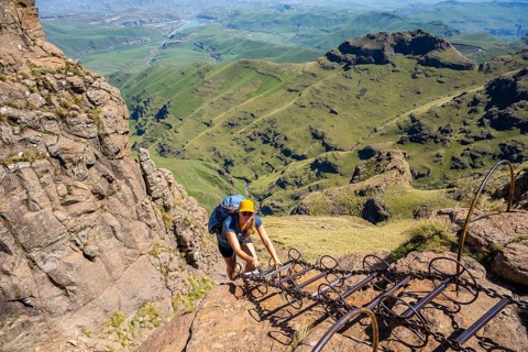 Young female hiker climbs over dangerous ladders, mountains and cliffs of the Drakensberg