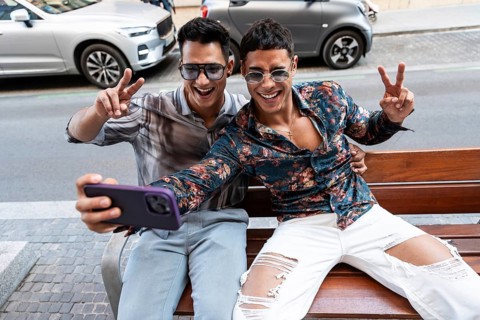 A cheerful latin gay couple takes a selfie on a sunny day in Madrid city, seated on a bench and