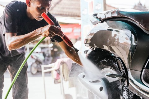 A man is meticulously cleaning a motorcycle with a water hose, showcasing the attention to detail