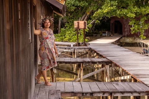 A tourist enjoys the serene beauty of Waigeo Island, Indonesia, standing on a rustic wooden walkway
