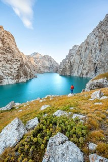 Young man at the turquoise mountain lake Kol Suu with rocky steep mountains, Kol Suu Lake, Sary