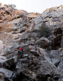 Two climbers takes on the challenge of a steep, rocky cliff in a rugged natural landscape. The