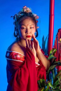 A woman in a red dress with a flower headpiece poses for a photo