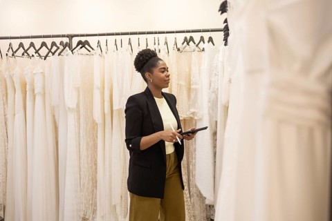 A woman stands in a bridal boutique, browsing a collection of elegant white wedding dresses. She