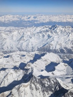 Stunning aerial view of a vast, snow-covered mountain range captured from an airplane, showcasing