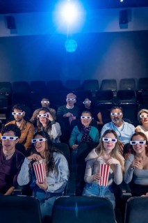 People of different ages wearing 3d glasses, eating popcorn and enjoying a movie in a cinema
