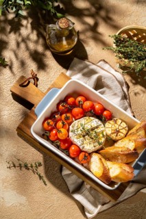 A rustic setting featuring baked Camembert cheese in a dish with cherry tomatoes, garlic, herbs,
