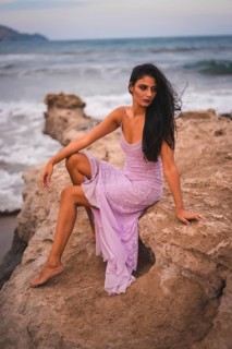 Posing of a young brunette Caucasian in a pink dress, on the beach having fun by the sea