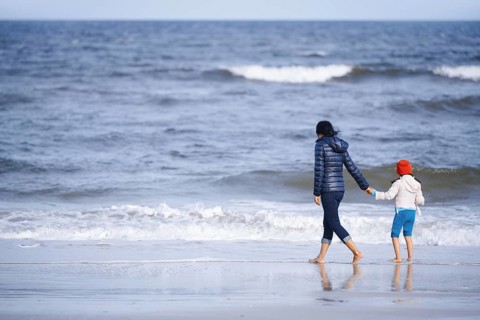 A mother and daughter holding hands, walking on a peaceful beach of California, United States. The