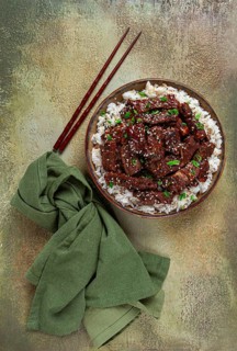 Crispy beef, with green onions and sesame seeds, on a rice pad, in a bowl with chopsticks, on a