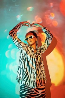 A young, trendy woman in bold zebra print clothing and white sunglasses poses against a vibrant,