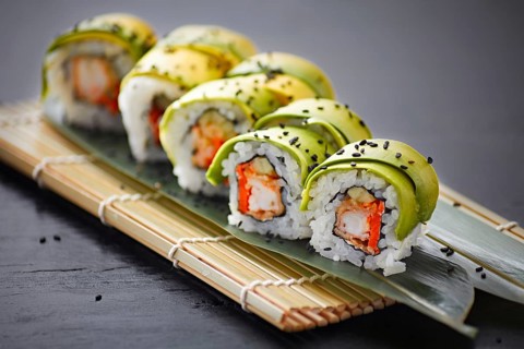 A delectable array of avocado-wrapped sushi rolls, topped with black sesame seeds, presented on a