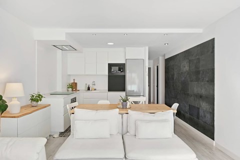 A chic, open concept kitchen and living area features sleek white cabinets, a natural wood table,