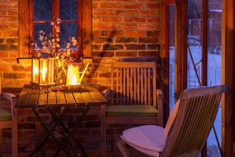 Still life in a winter garden with candles on a table next to chairs, outside you can see the