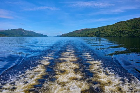 Boat waves on a river with wooded hills and blue sky in the background, Fort Augustus, Loch Ness,