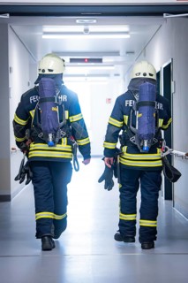 Two firemen in full equipment move through a corridor, fire brigade exercise on blue light day in