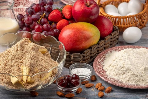 Bowl with baking ingredients next to eggs, milk and a basket of fruit