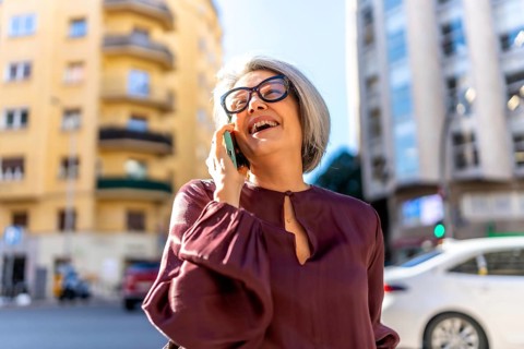 Senior woman enjoying a lively conversation on her smartphone, smiling and laughing outdoors in an