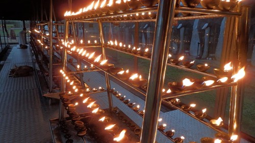 Rows of burning oil lamps at a spiritual ceremony create a mystical atmosphere in front of a
