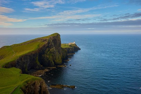 A lighthouse at the top of a green cliff overlooking the blue sea and sky, Neist Point Lighthouse,