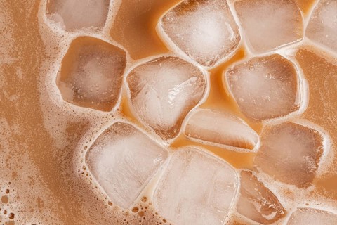 A detailed top-down view of iced cold brew coffee, showcasing ice cubes floating in the brew. The