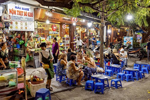 Lively Asian night market with food stalls and people on blue stools under trees and colourful