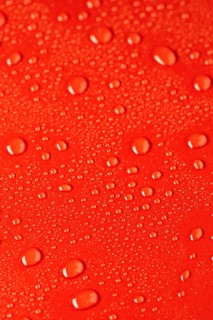 Close up of water droplets scattered on a vibrant red surface, creating a dynamic texture. The