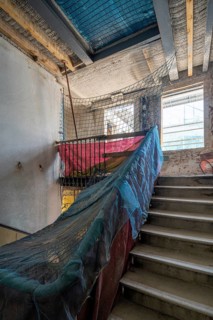 Sunlit construction site with stairs, partially covered with protective nets. Exposed beams and