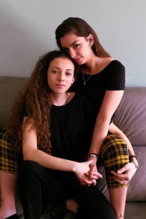 A tender portrait of a female gay couple embracing on a sofa. Both women gaze lovingly into the