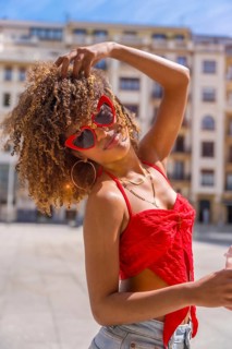 Vertical photo of a lovely latin young woman in summer clothes and funny red heart shape sunglasses