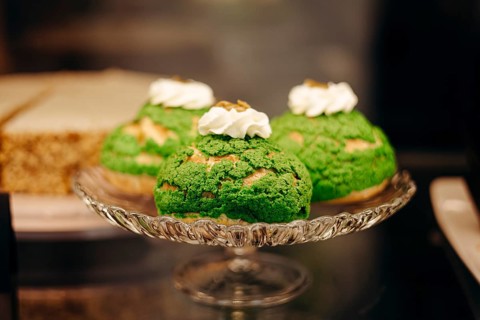 A display of vibrant matcha choux pastries with whipped cream on an elegant glass plate, set in a