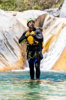 Man stands in shallow river in full canyoneering gear, surrounded by smooth rock formations and