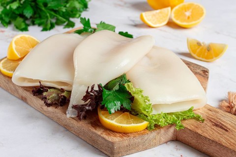 Fresh squid prepared for cooking, surrounded by herbs and lemon, placed on a wooden chopping board