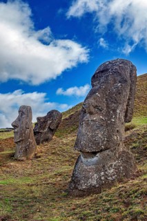 Large stone sculptures on a grassy hill under a cloudy blue sky, The Moai Statues on Easter Island