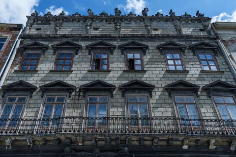 Dilapidated residential building with balcony and sculptures on the roof ledge, 19th century,