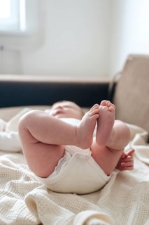 A serene image of a newborn baby girl lying on a soft, knitted blanket. Her tiny feet are playfully