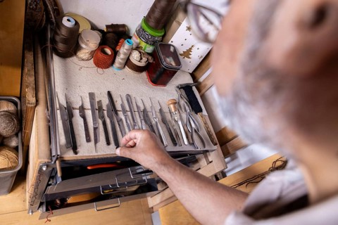 Cropped unrecognizable Iranian carpet restorer chooses tools in his Salzburg workshop, surrounded