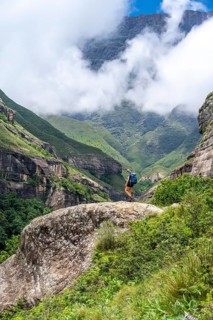 Female hiker standing in front of landscape with mountains and fog, Drakensberg National Park,