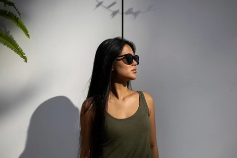 Chinese woman in sunglasses standing against a sunlit wall, basking in the summer glow, embodying