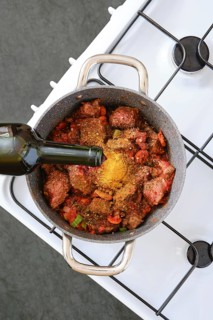 A pot filled with diced meat, chopped vegetables, and spices is being prepared on a sleek stovetop.