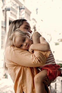 A loving mother embraces her young daughter outside. The mother holds her child gently, creating a