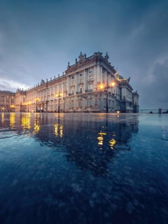 Majestic Royal Palace of Madrid with illuminated facade in twilight. The architecture is mirrored